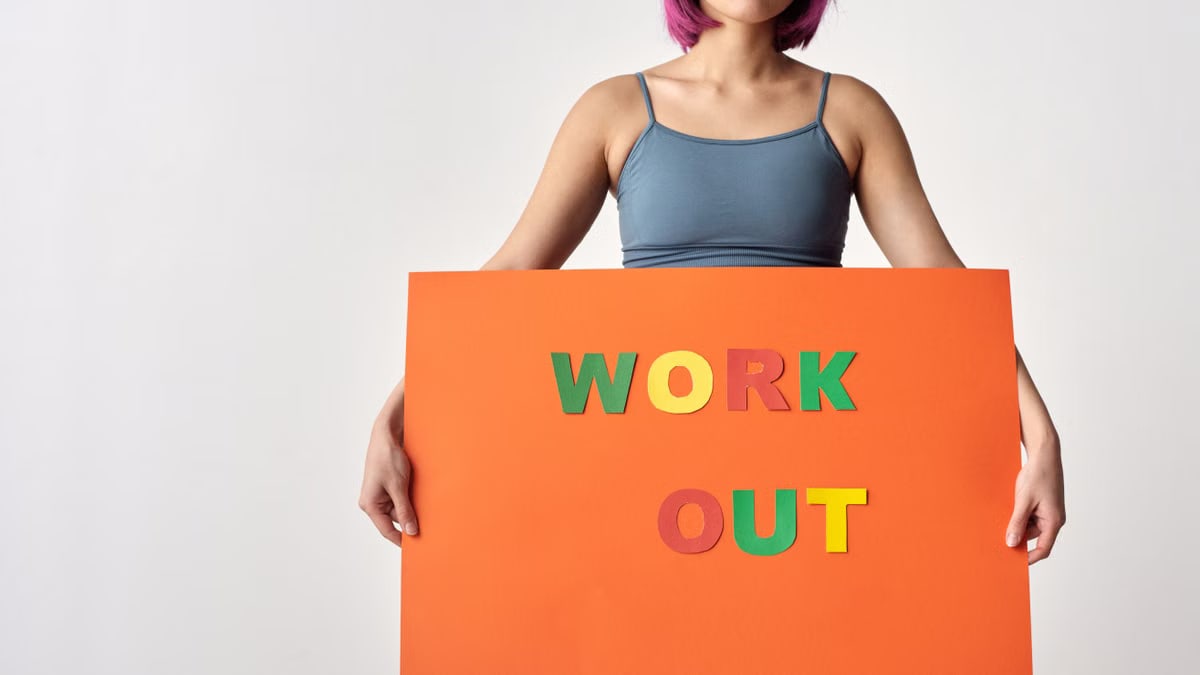 Woman with short hair holding a vibrant 'Work Out' sign on a white background.